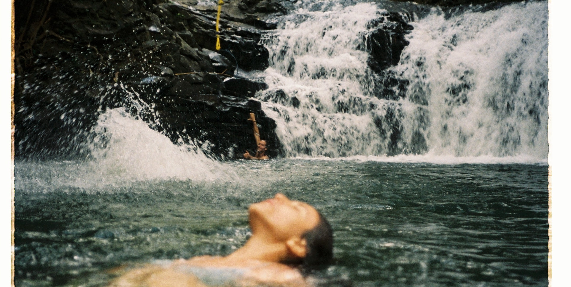 A woman floating in a waterfall lake with a waterfall behind her