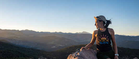 A woman sitting on a rock at the top of a mountain looking out on sunset