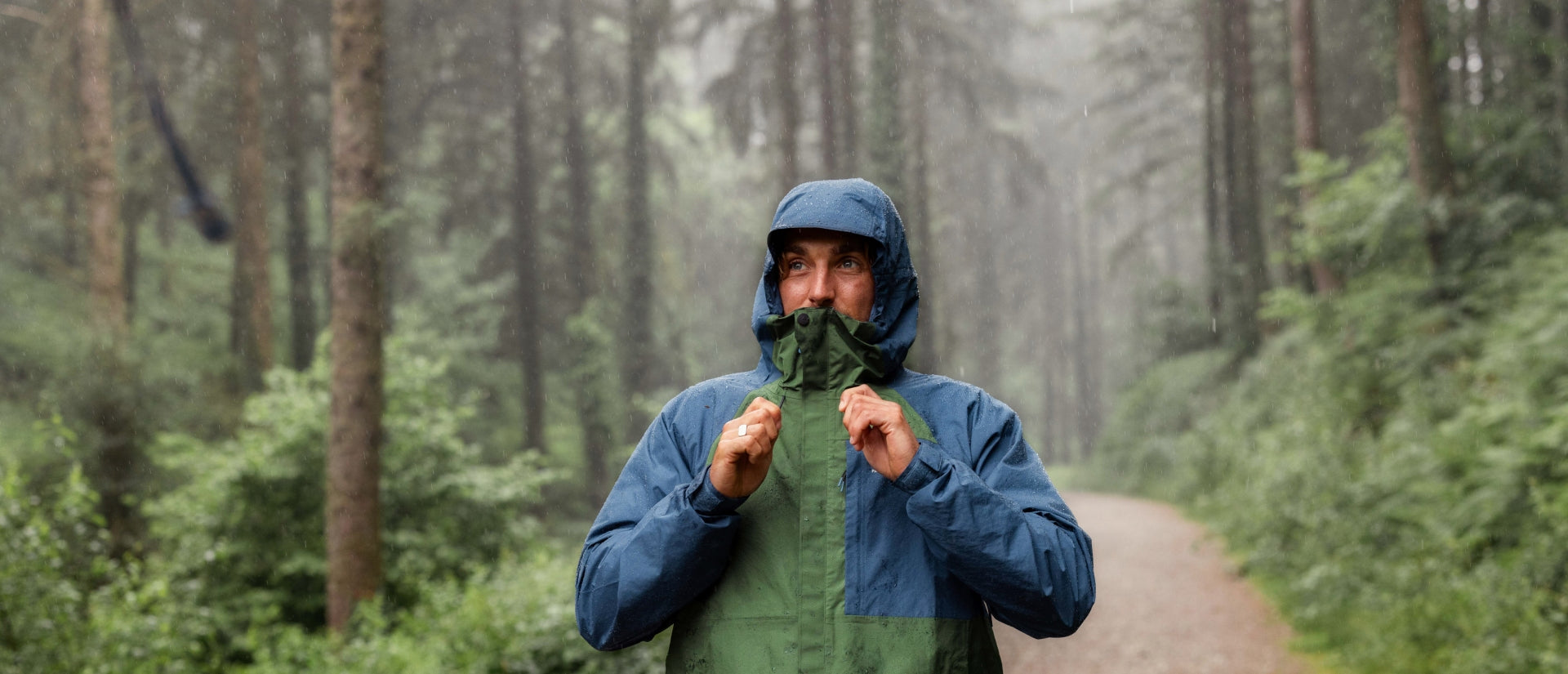 A man with his hood up, pulling on his drawstrings as the rain comes down
