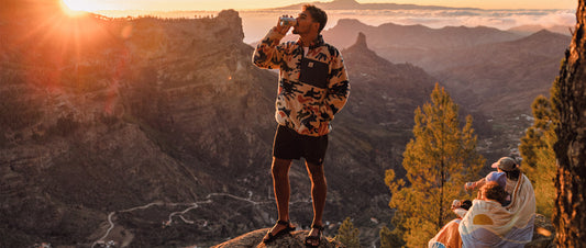 A man sipping from a can overlooking the valley below at sunset