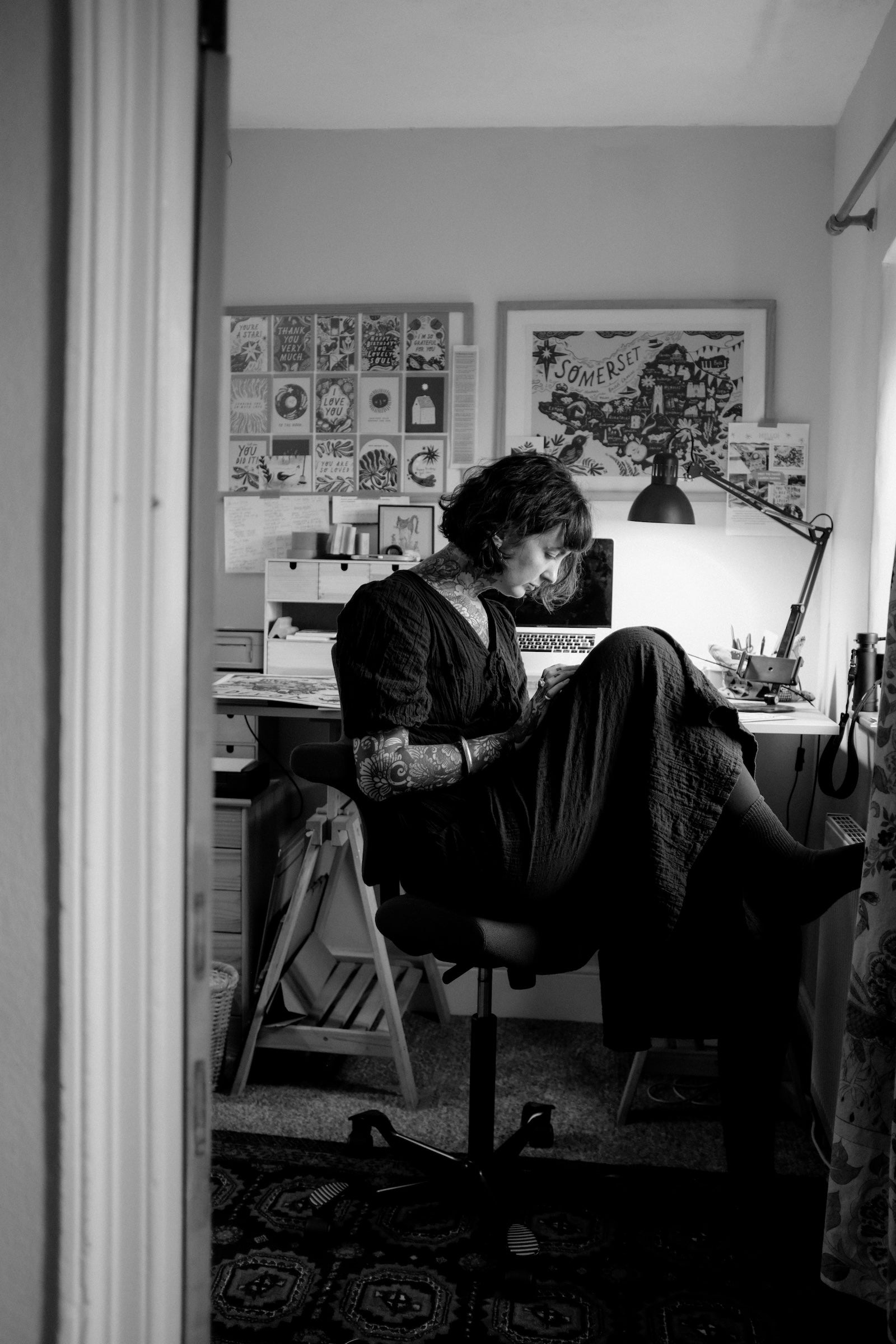 Person sitting at a desk in a home office with various items on the wall and desk.